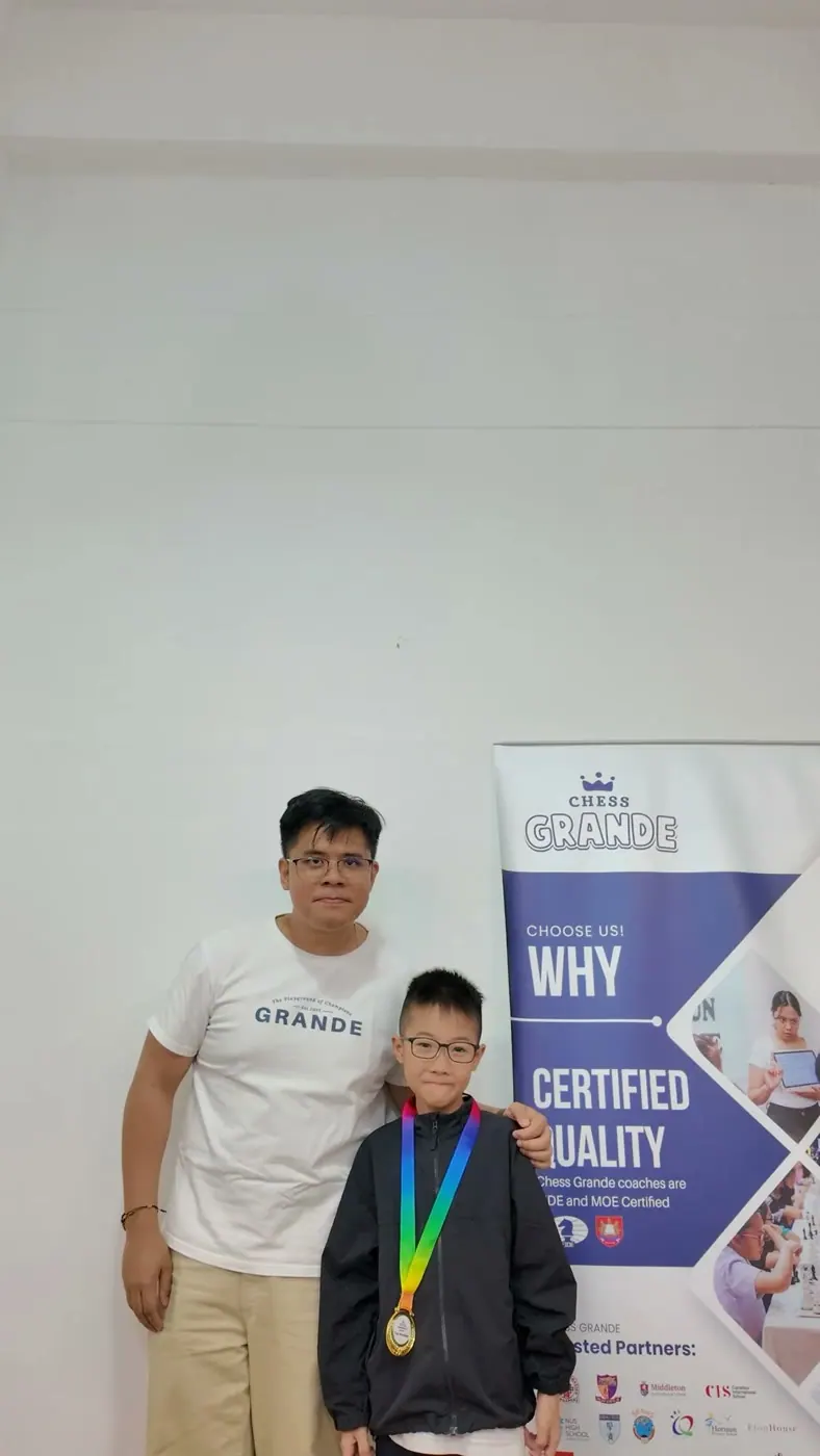 A meetup participant posing with a medal beside the Chess Grande display