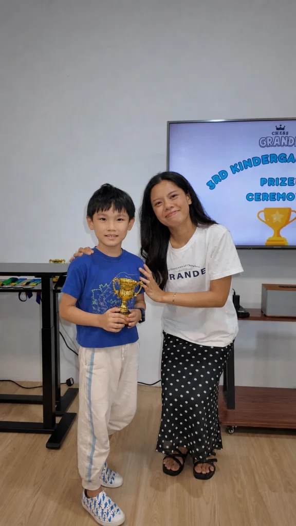 A Kindergarten Cup prize winner holds a trophy beside a family member.