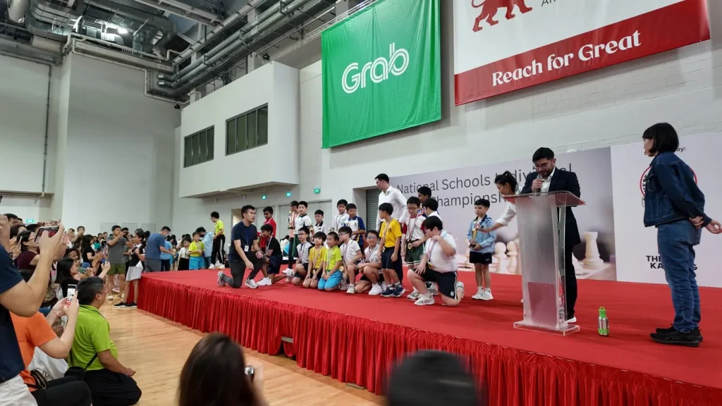 Young school chess players gather on stage during a tournament awards ceremony.