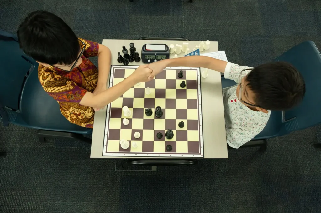 Two young players shake hands across the board at a school chess tournament.